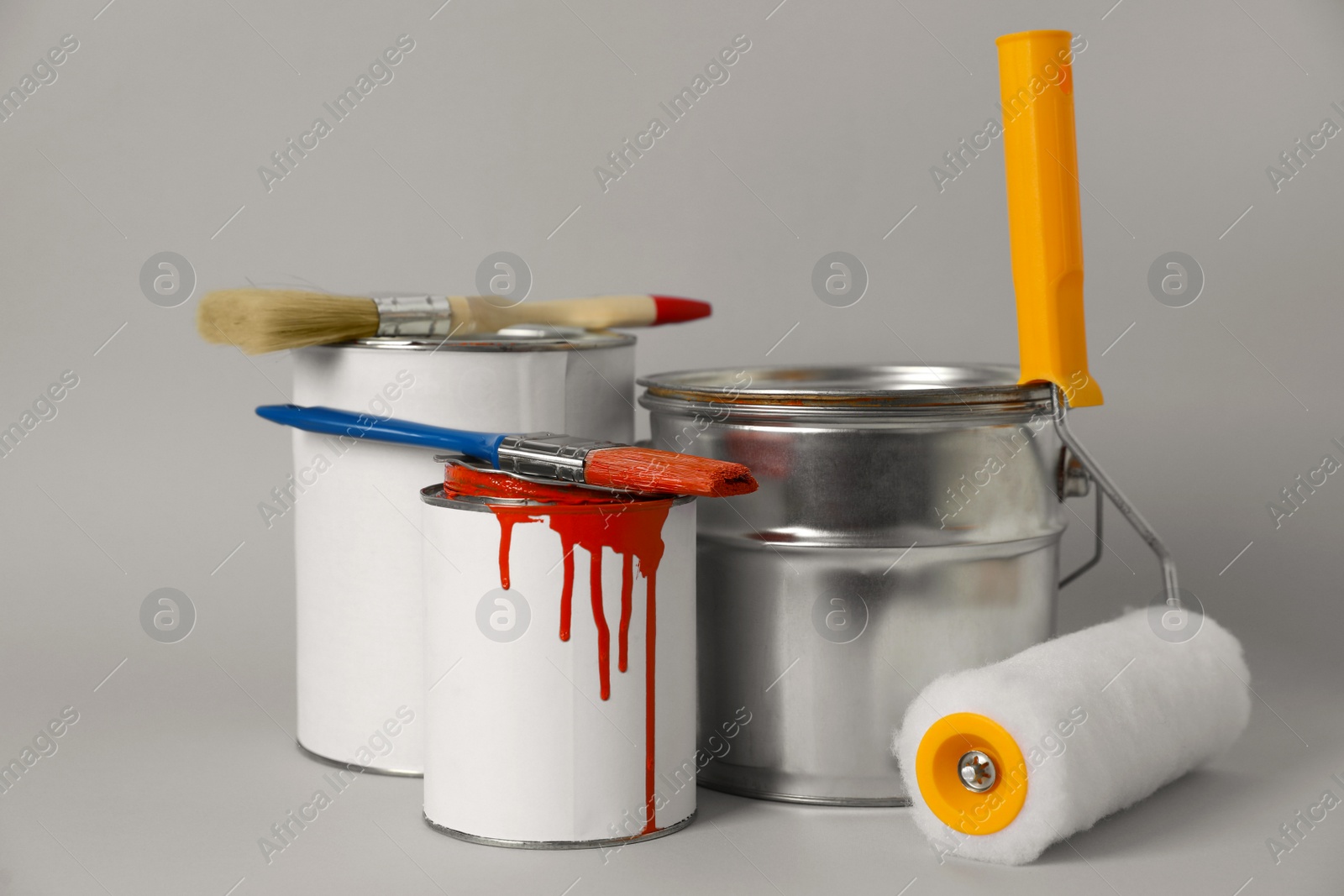 Photo of Cans of orange paint, brushes and roller on grey background