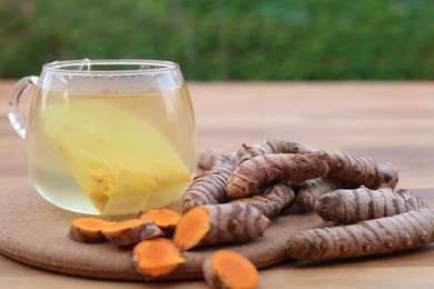 Glass cup of hot tea and fresh turmeric roots on wooden table, closeup
