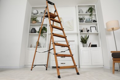Photo of Wooden folding ladder near chest of drawers and shelves with accessories in room, low angle view