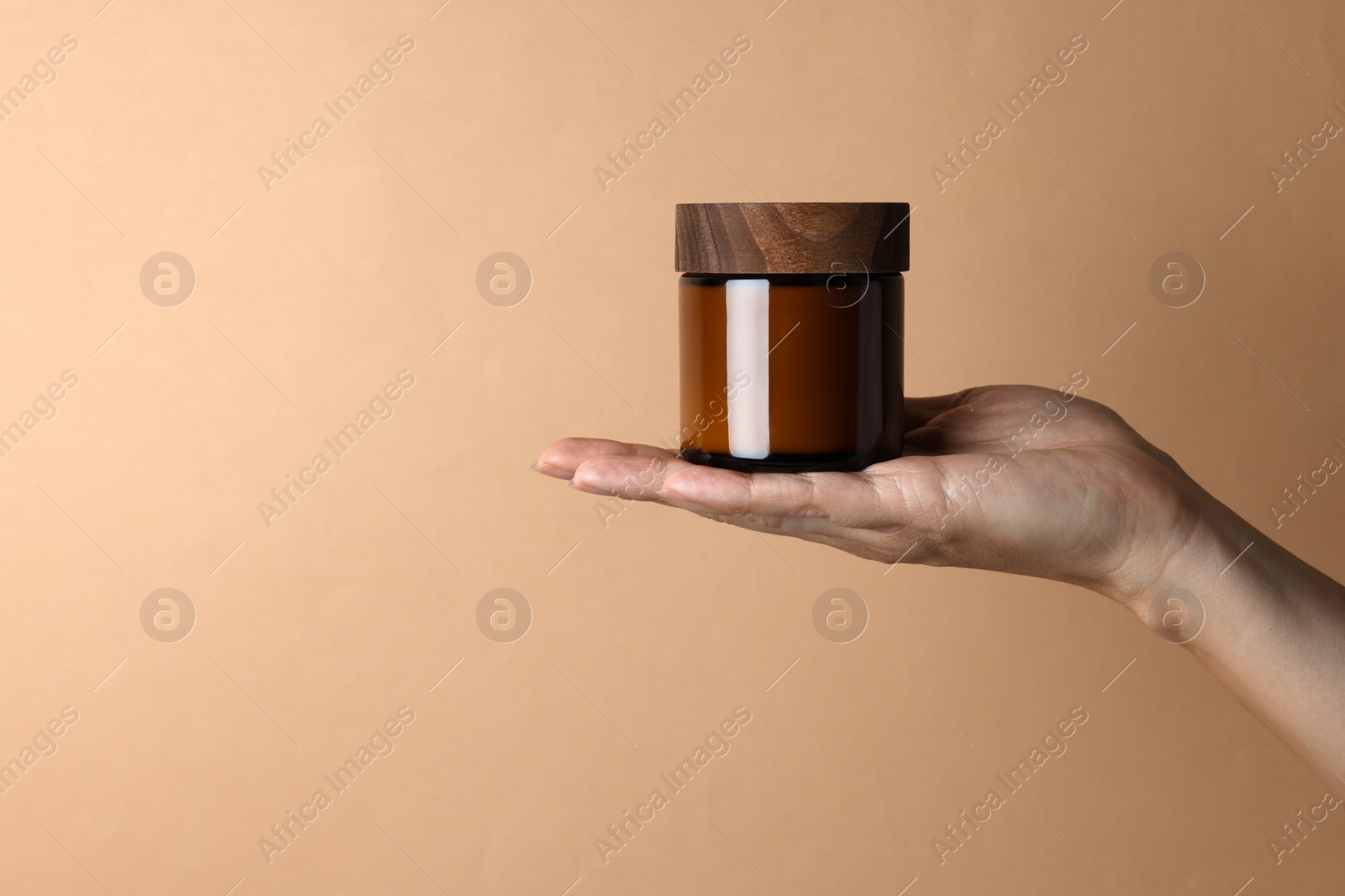 Photo of Woman holding jar of cosmetic product on beige background, closeup. Space for text