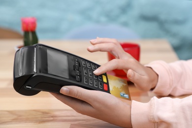 Photo of Woman using card machine for non cash payment at table, closeup