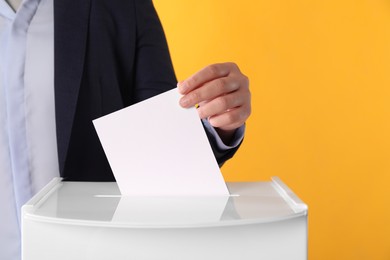 Photo of Woman putting her vote into ballot box on orange background, closeup