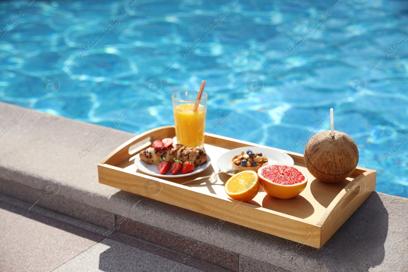 Photo of Tray with delicious breakfast near swimming pool