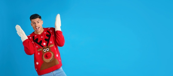 Photo of Excited man in Christmas sweater and mittens on blue background, space for text