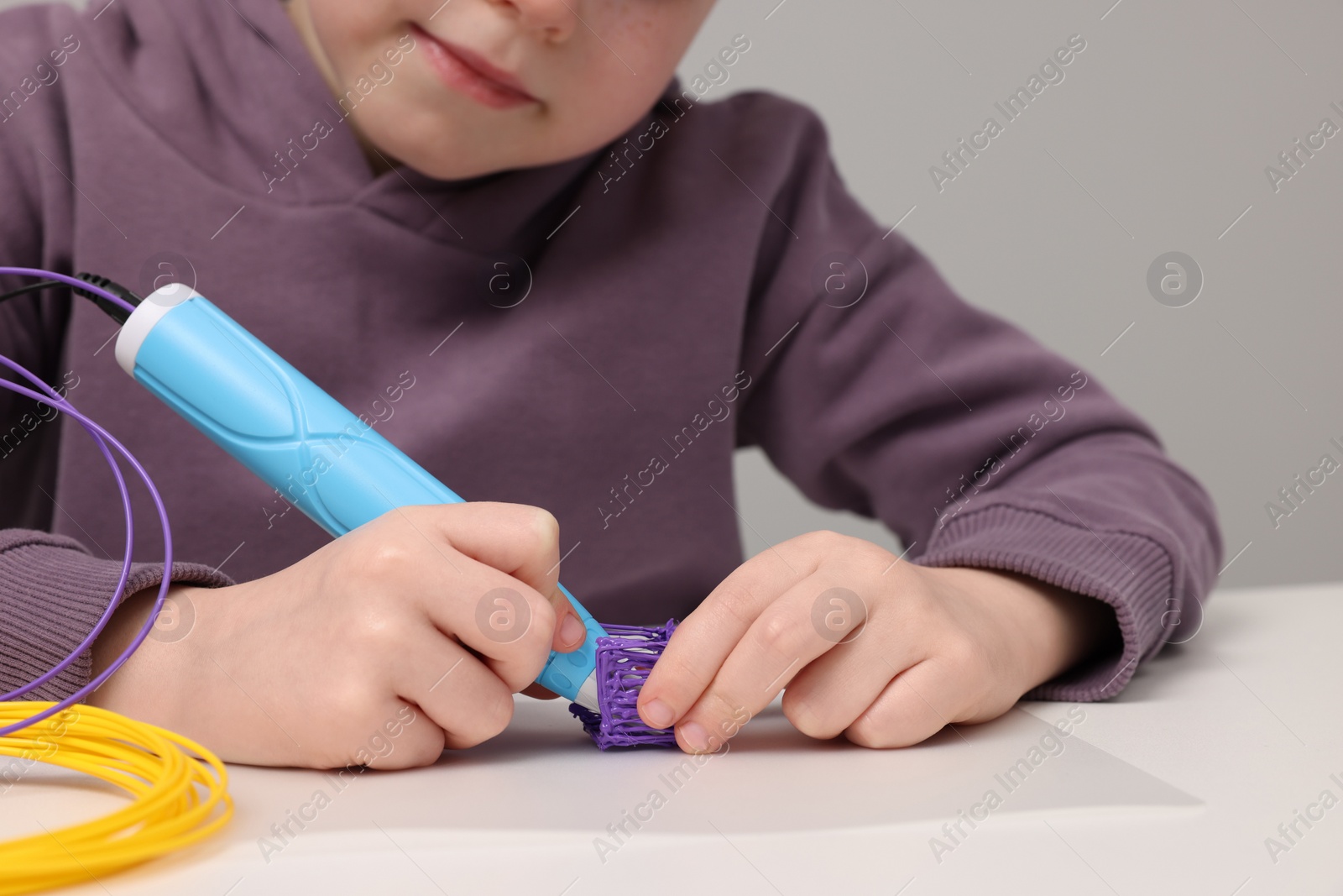 Photo of Boy drawing with stylish 3D pen at white table, closeup