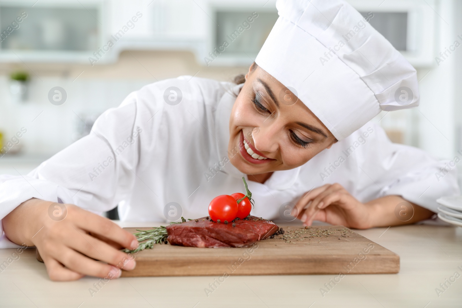 Photo of Professional female chef cooking meat on table in kitchen