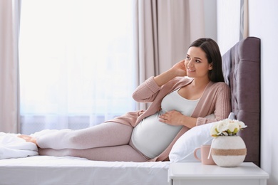 Photo of Young beautiful pregnant woman lying on bed and touching her belly at home