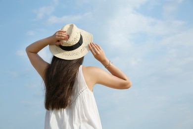 Photo of Beautiful young woman wearing straw hat outdoors, back view. Stylish headdress