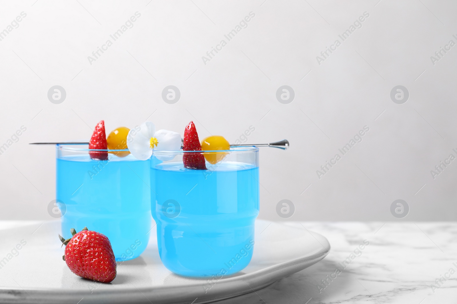 Photo of Bright light blue cocktail in glasses on white marble table, space for text