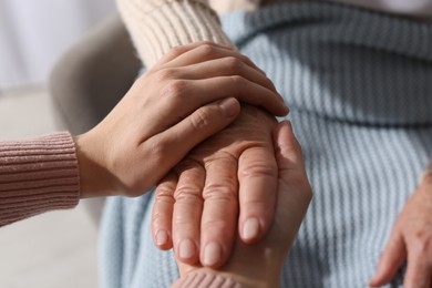 Photo of Young and elderly women holding hands together indoors, closeup