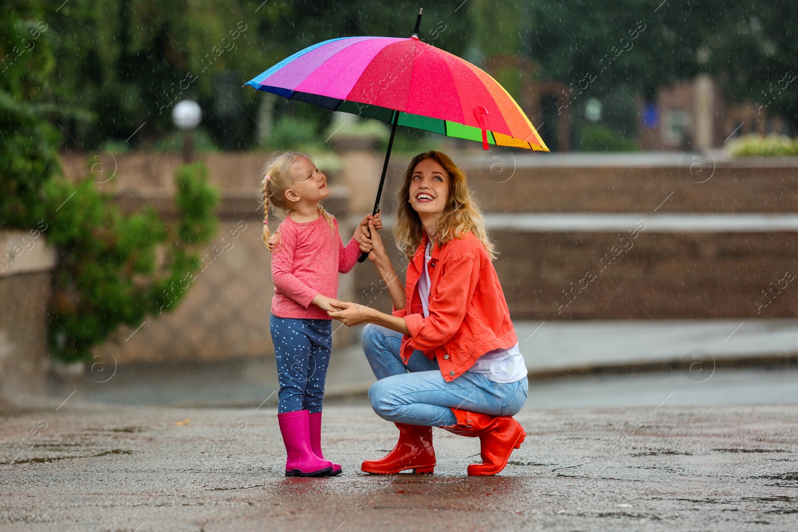 Photo of Happy mother and daughter with bright umbrella under rain outdoors