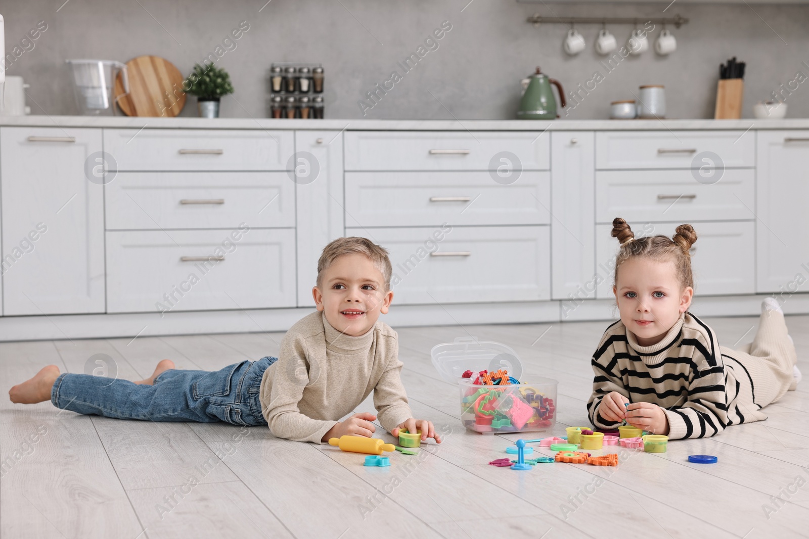 Photo of Cute little children playing together on warm floor in kitchen. Heating system