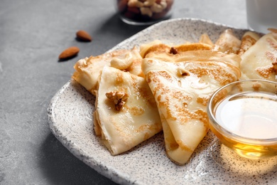 Photo of Thin pancakes served with honey on plate, closeup