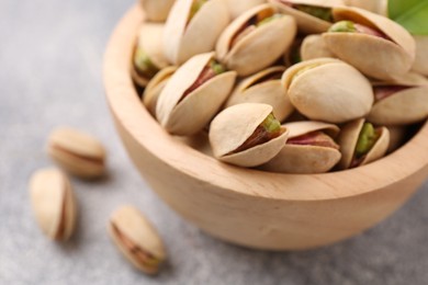 Delicious pistachios in bowl on grey textured table, closeup