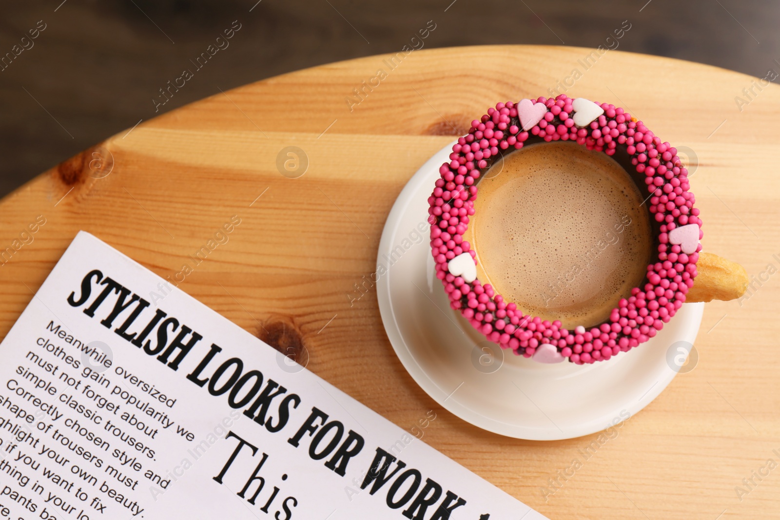Photo of Delicious edible biscuit cup of coffee decorated with sprinkles and newspaper on wooden table, flat lay