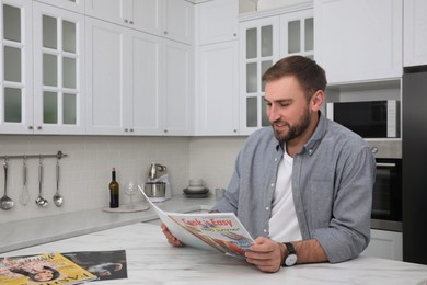 Photo of Handsome man reading magazine at white marble table in kitchen