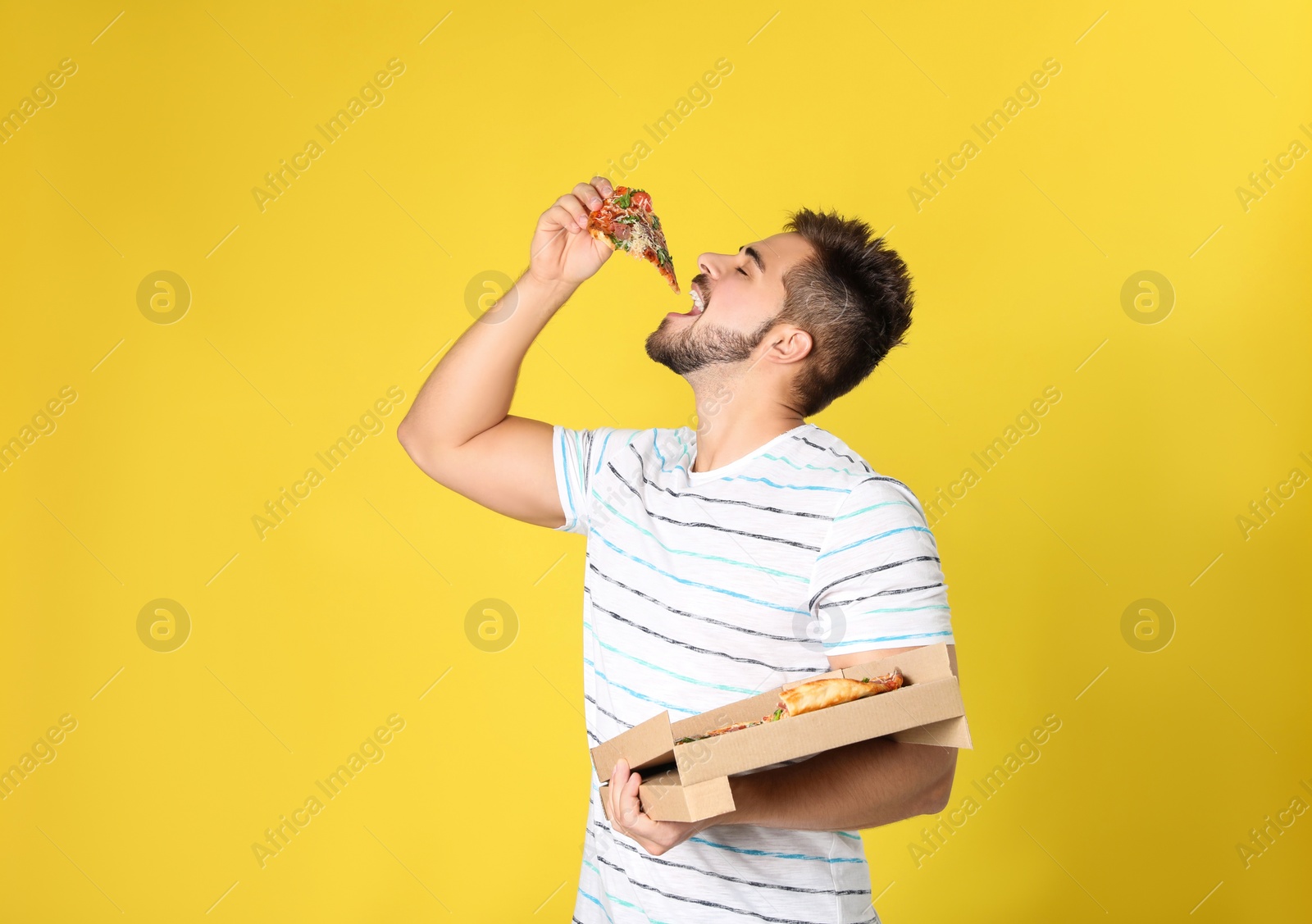 Photo of Handsome man eating tasty pizza on yellow background