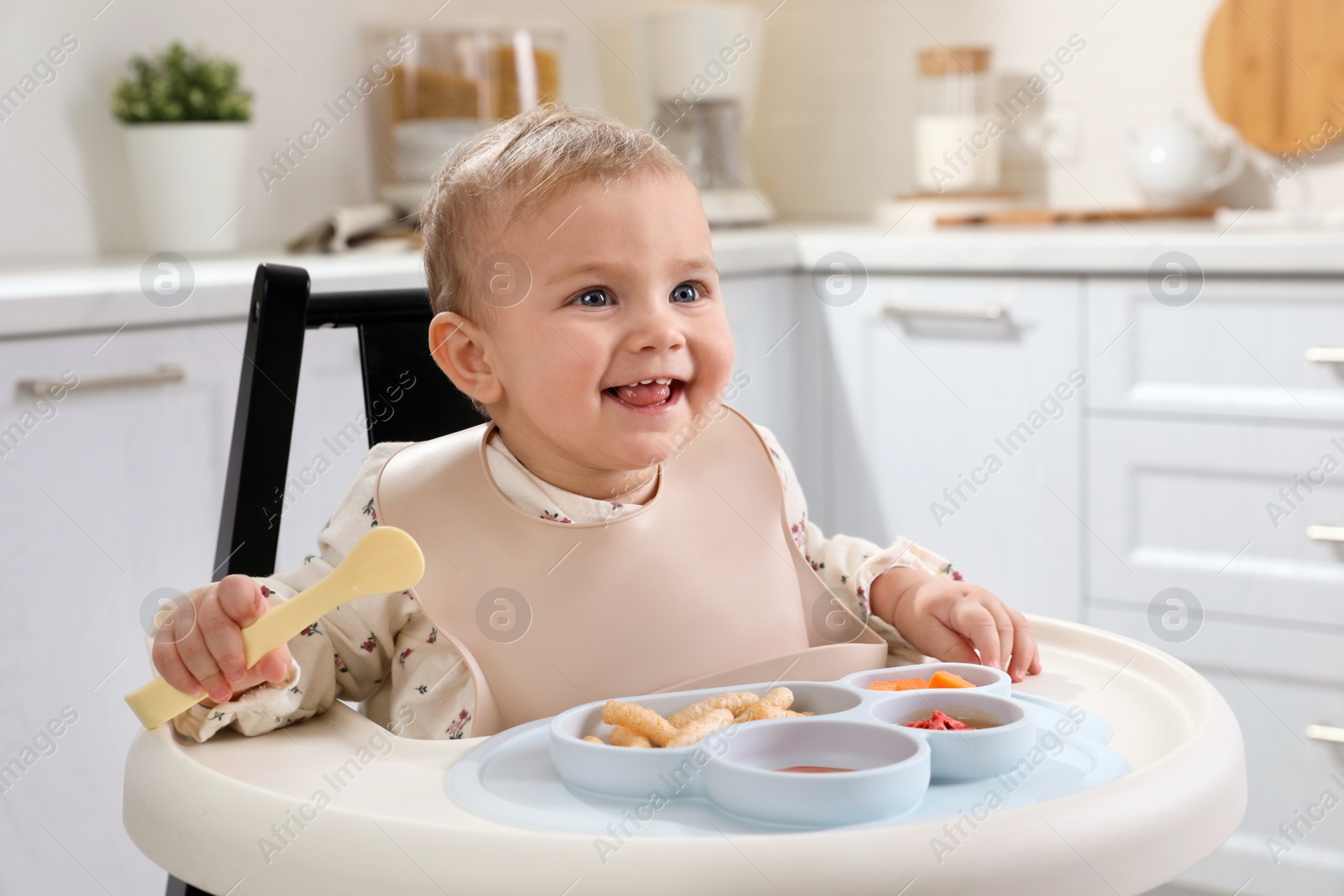 Photo of Cute little baby eating food in high chair at kitchen