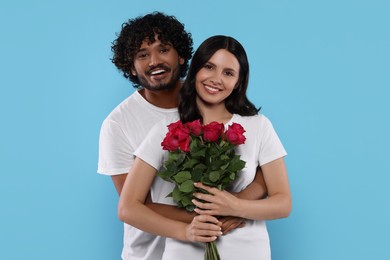 Photo of International dating. Happy couple with bouquet of roses on light blue background