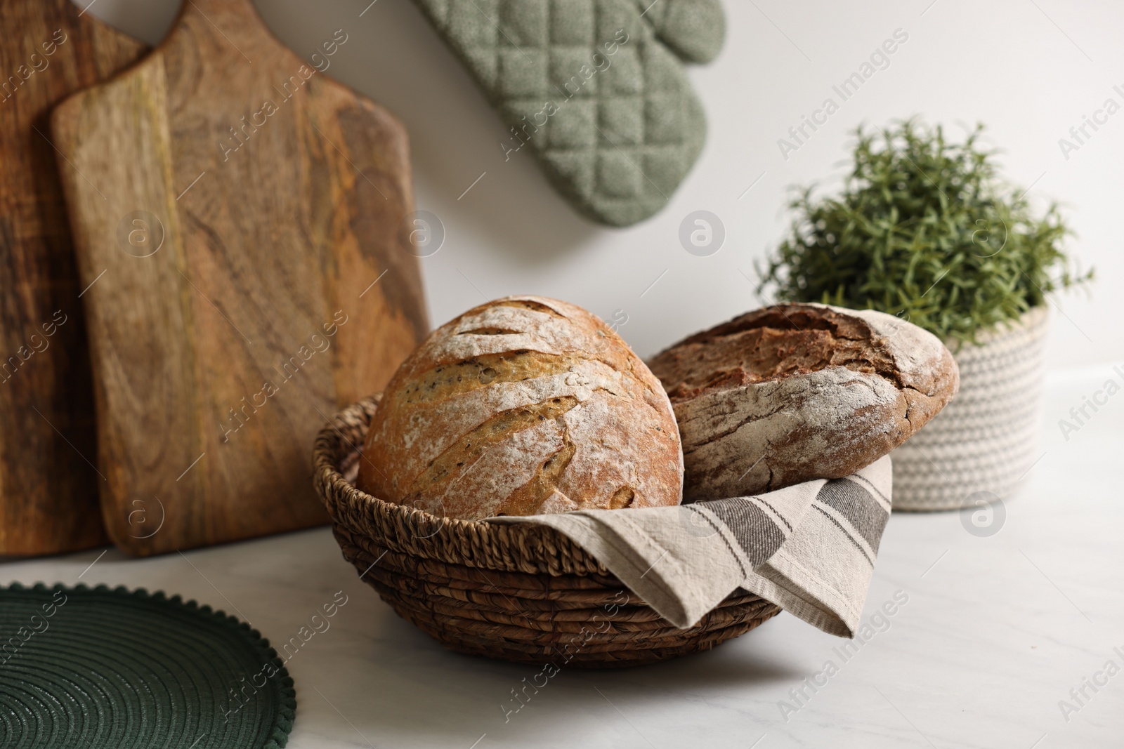 Photo of Wicker bread basket with freshly baked loaves on white marble table in kitchen