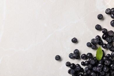 Photo of Ripe bilberries and leaf on light marble table, flat lay. Space for text