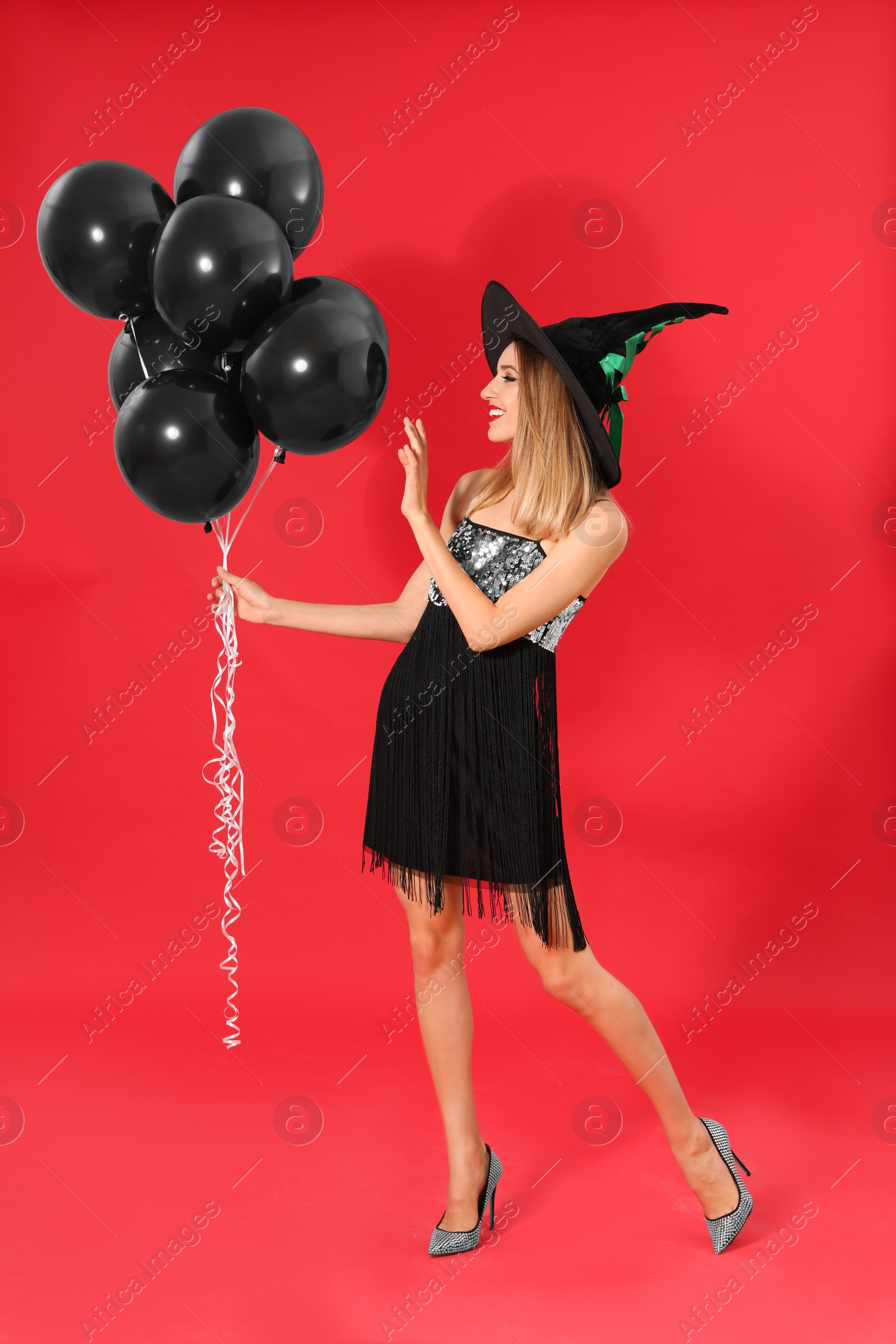 Photo of Beautiful woman wearing witch costume with balloons for Halloween party on red background