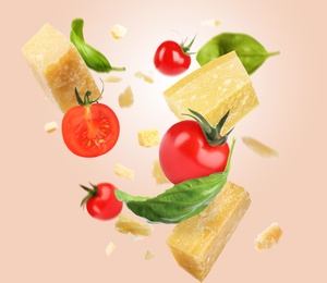 Pieces of delicious parmesan, tomatoes and basil leaves falling on beige background