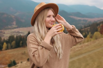 Photo of Young woman with mug of hot drink in mountains. Space for text