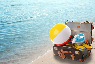 Image of Suitcase with different beach objects on sand near sea. Space for text