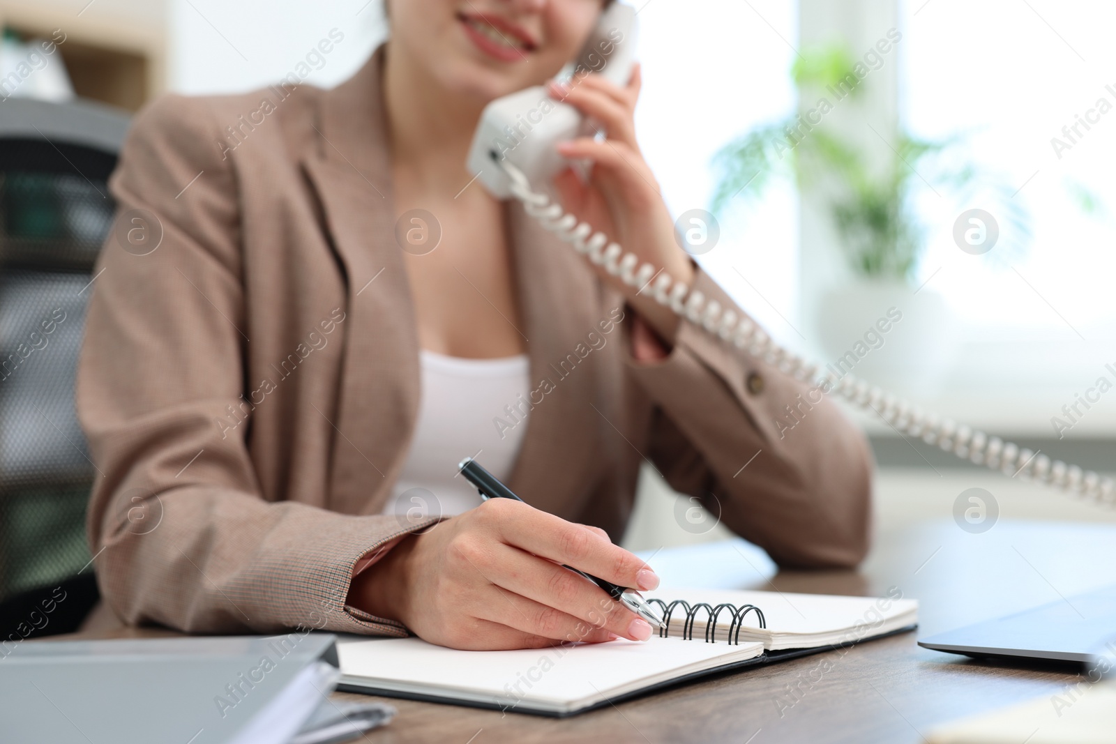 Photo of Smiling secretary talking on telephone at table in office, closeup