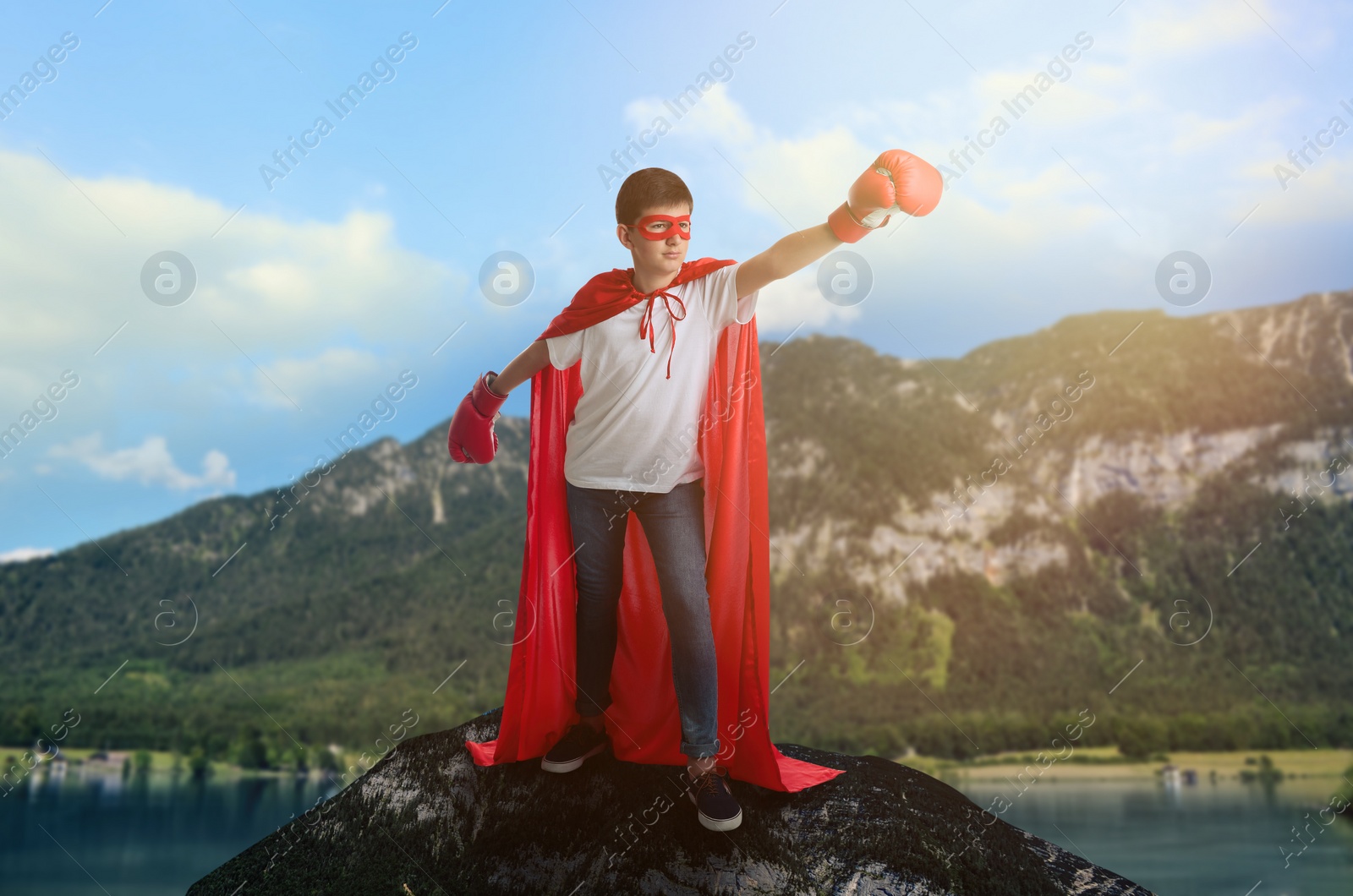 Image of Superhero, motivation and power. Boy in cape and mask wearing boxing gloves on high top in mountains
