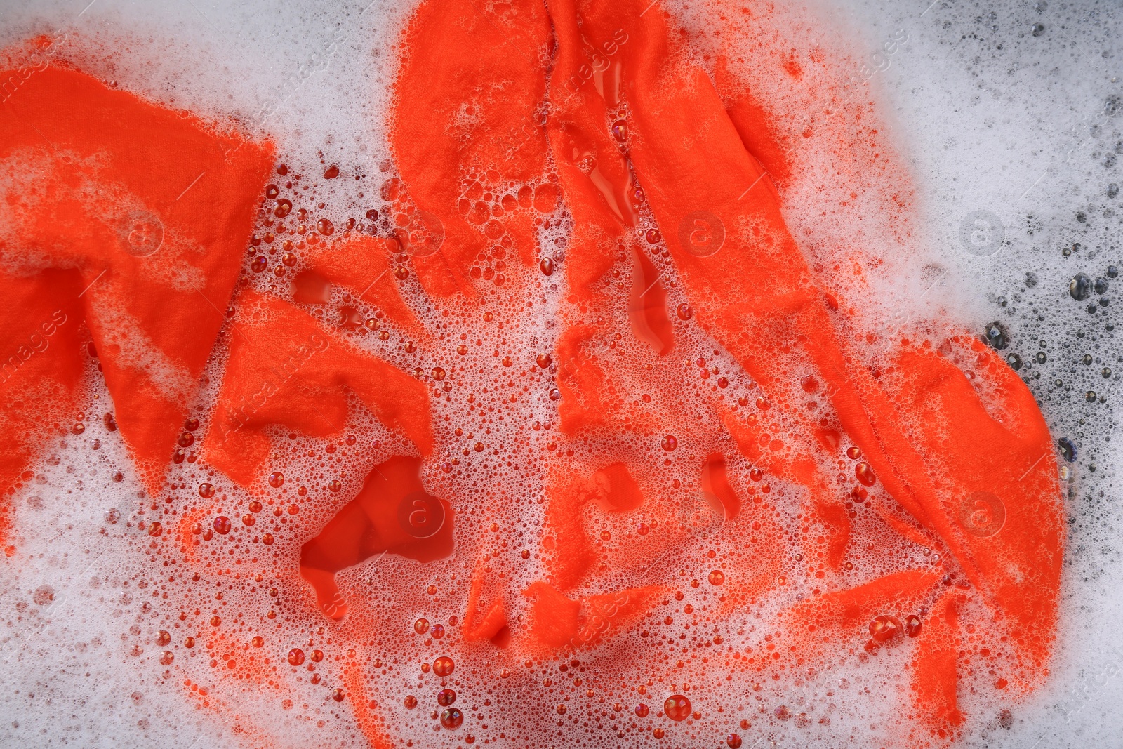 Photo of Orange garment in suds, top view. Hand washing laundry