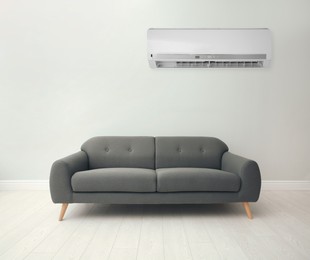 Image of Modern air conditioner on white wall in room with stylish grey sofa