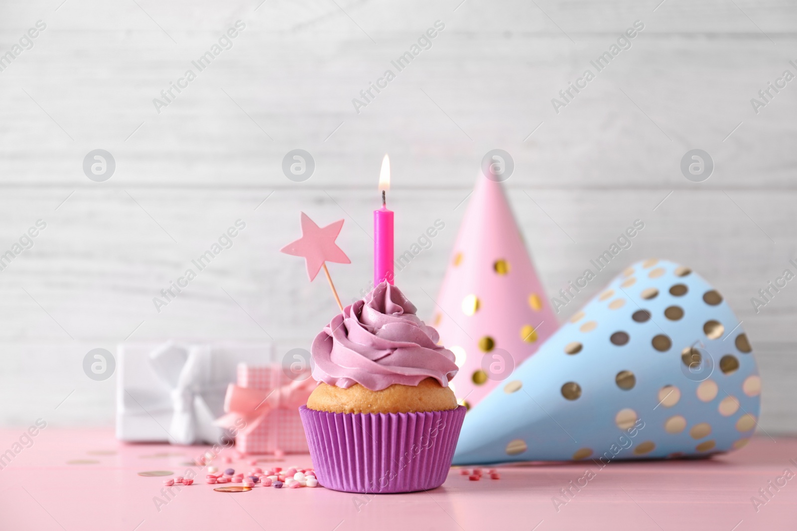 Photo of Birthday cupcake with burning candle, party hats and gift boxes on pink table