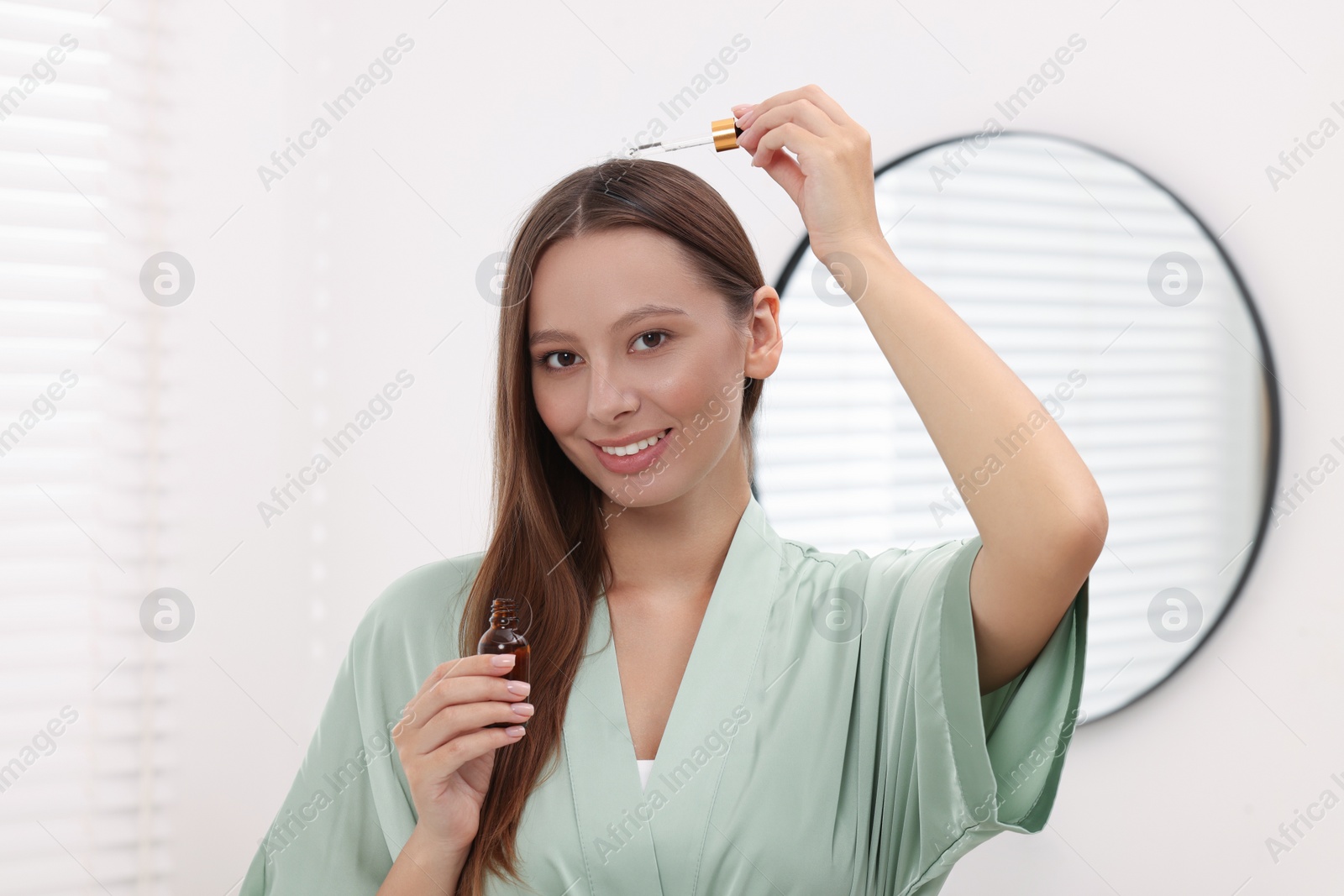 Photo of Beautiful woman applying serum onto hair indoors