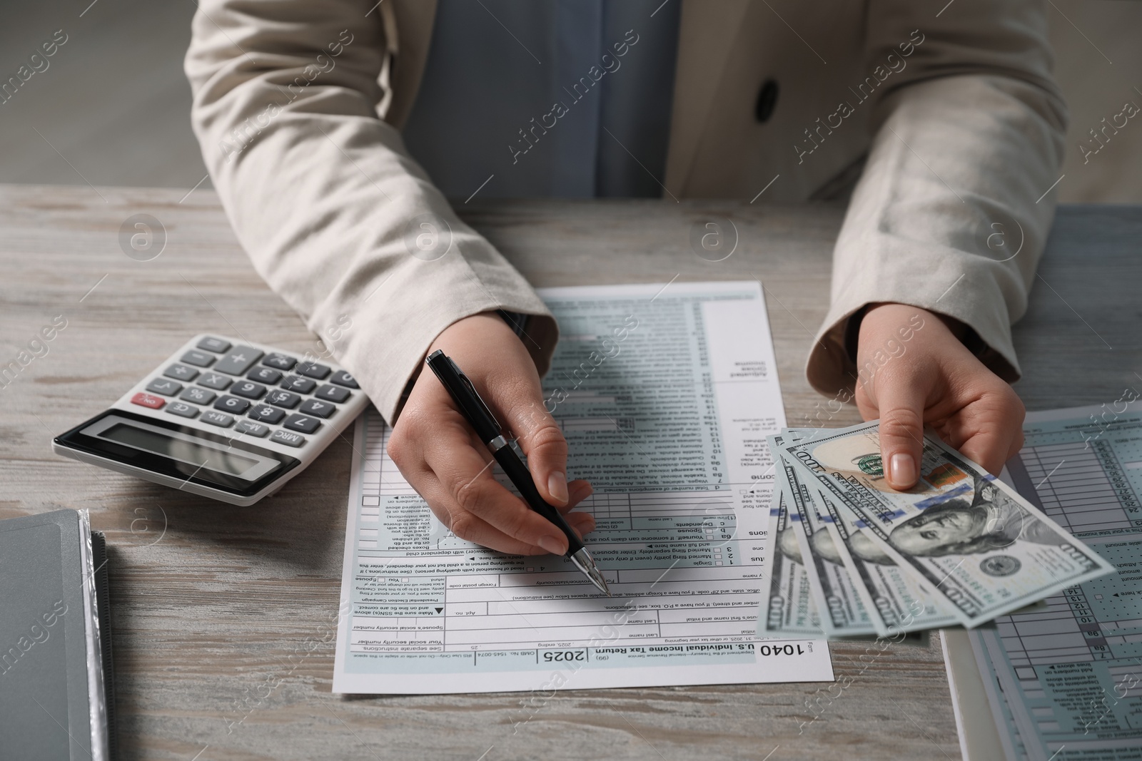 Photo of Payroll. Woman with dollar banknotes working with tax return forms at wooden table, closeup