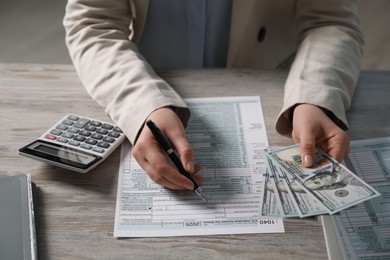 Payroll. Woman with dollar banknotes working with tax return forms at wooden table, closeup