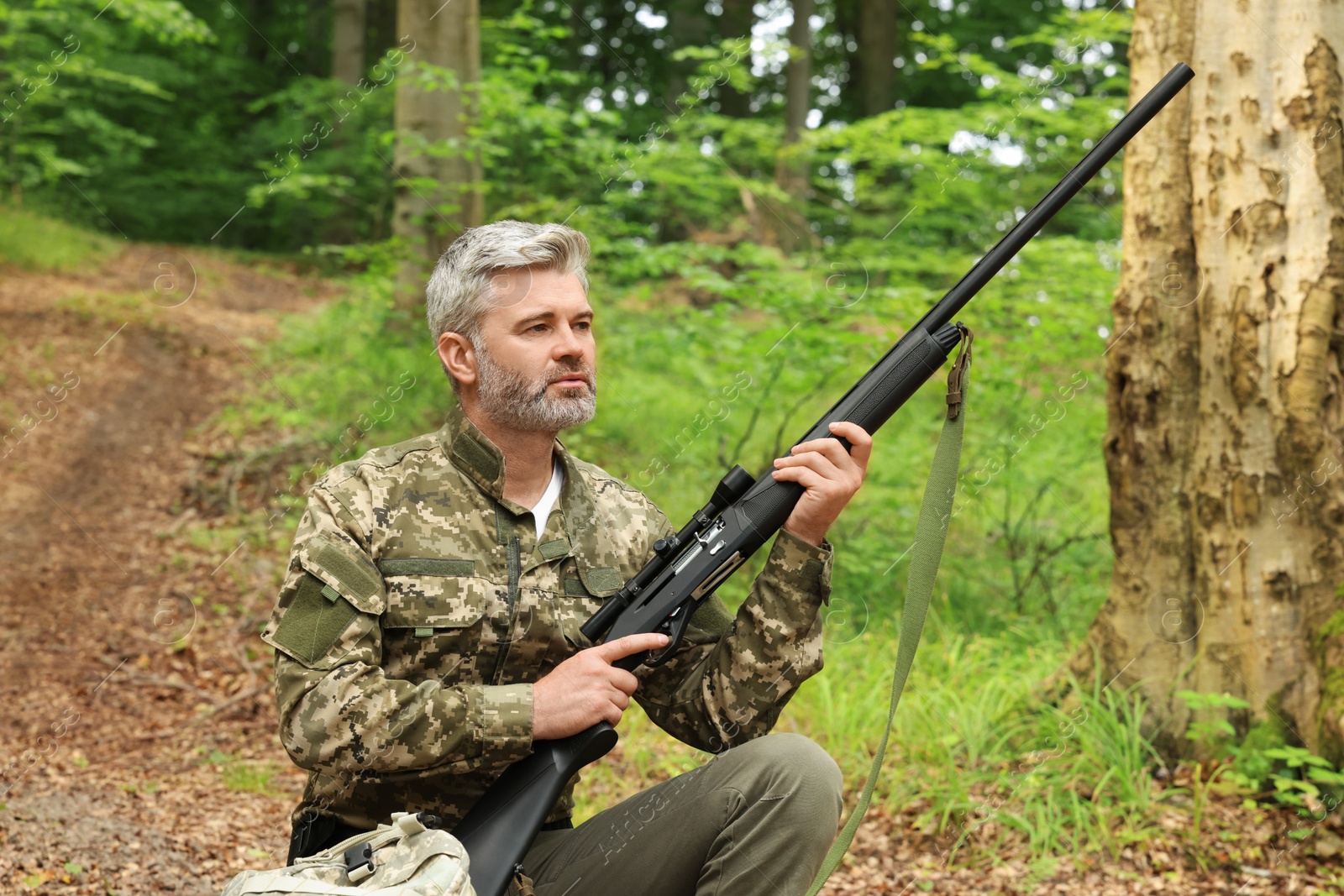 Photo of Man with hunting rifle and backpack wearing camouflage in forest