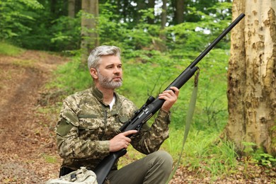 Photo of Man with hunting rifle and backpack wearing camouflage in forest