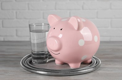 Water scarcity concept. Piggy bank, shower hose and glass of drink on wooden table