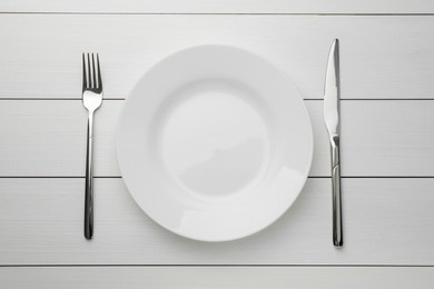 Photo of Clean plate, fork and knife on white wooden table, top view
