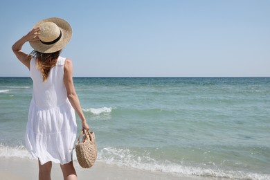 Woman with beach bag and straw hat near sea, back view