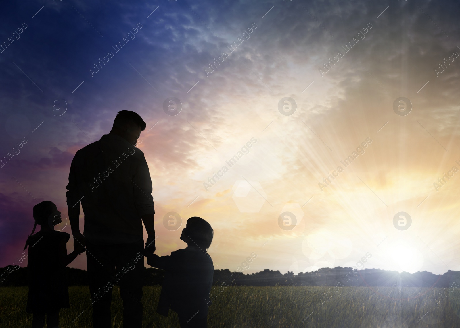 Image of Silhouettes of godparent with children in field at sunrise