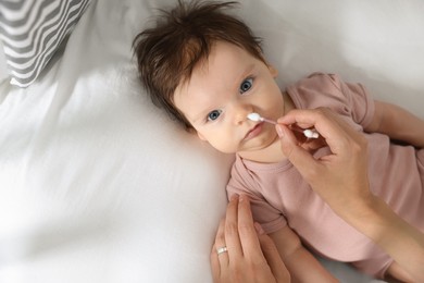 Photo of Mother cleaning nose of her baby with cotton bud on bed, top view