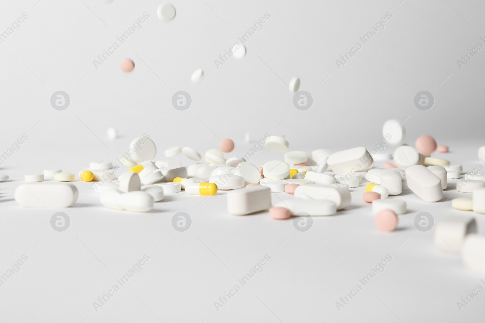 Photo of Different pills falling on table against white background