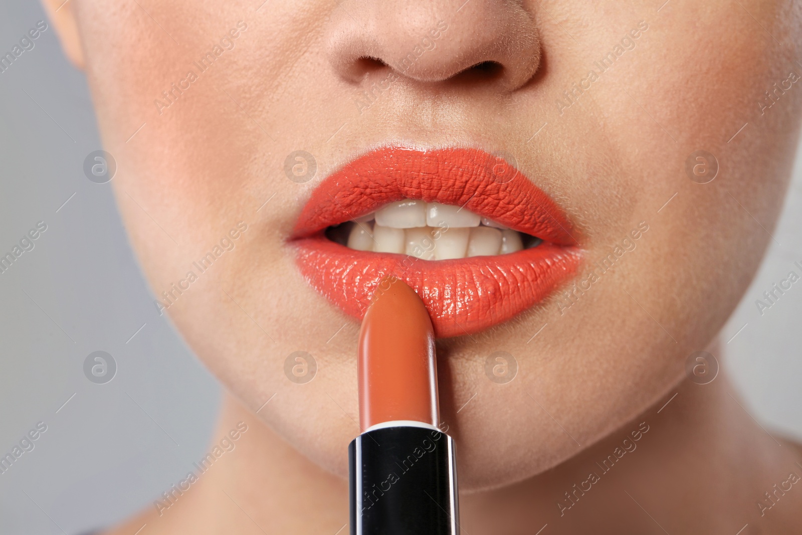 Photo of Young woman applying beautiful lipstick on gray background, closeup