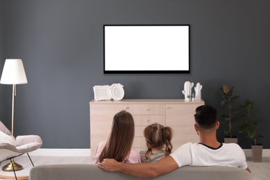 Photo of Family watching TV on sofa at home, back view