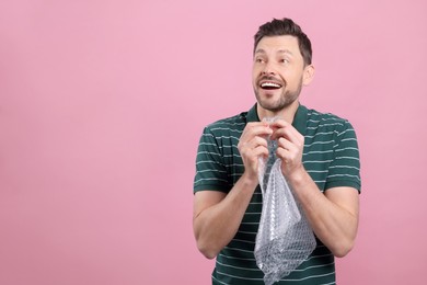 Happy man popping bubble wrap on pink background, space for text. Stress relief