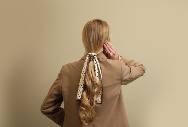 Young woman with stylish bandana on beige background, back view