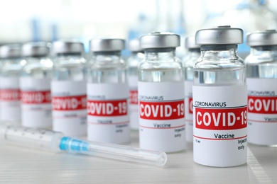 Photo of Glass vials with COVID-19 vaccine and syringe on white wooden table